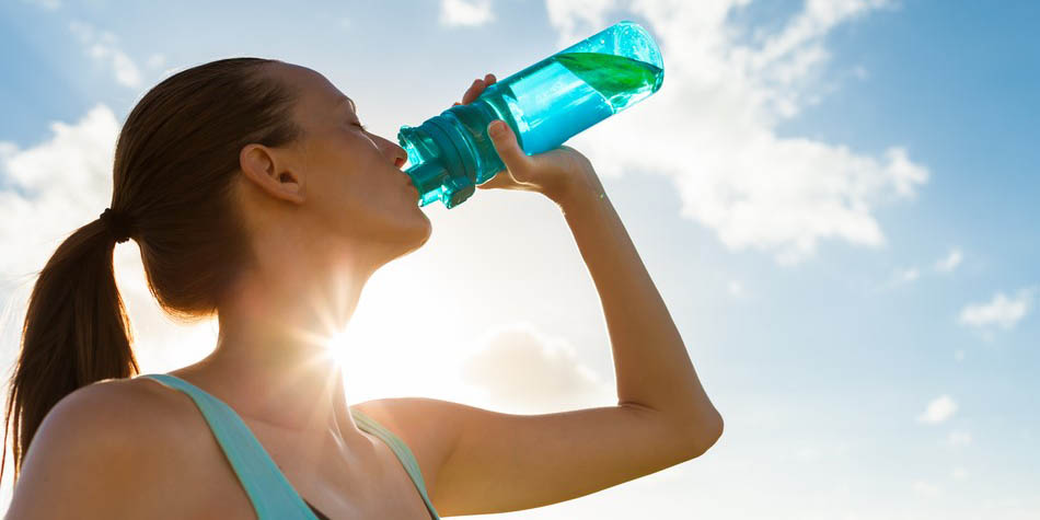 A woman drinks from a bottle of water outside in the sun.
