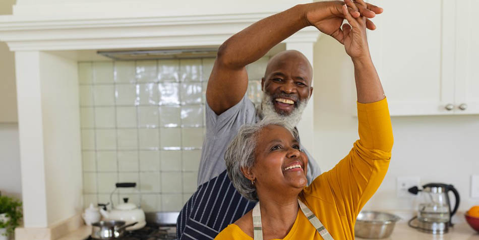 An older couple dances in the kitchen.